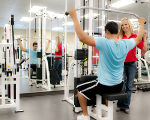 A man working out in the Wellness Center, and a woman looking on.
