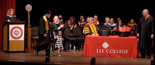 A graduating dad walks across the stage with his young daughter.