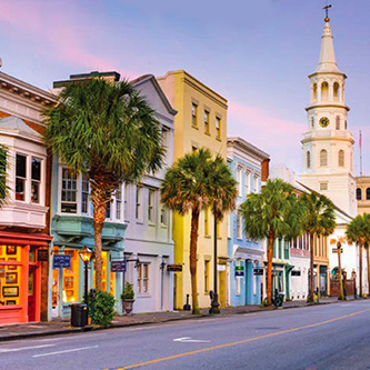 A row of beautiful old buildings, including a church with steeple, on a street lined with palm trees